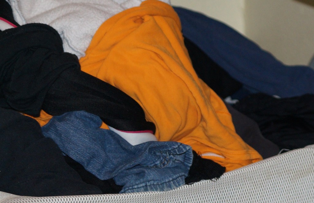 a pile of laundry in a mesh carrier: orange shirt, jeans, sweatshirt and more jumbled together.