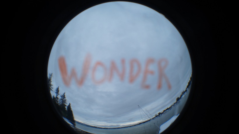 A fish-eye lens view of the lake and sky with the word "WONDER" in orange floating in the clouds.