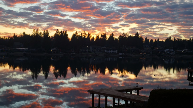 A reflection of pink clouds and dark trees on the lake.
