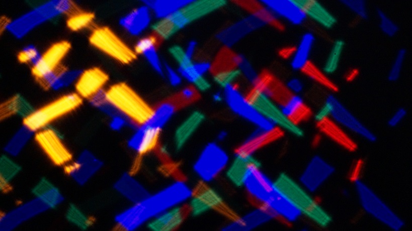 An abstract photograph of over lapping triangles in yellow, green, blue, and red that could be seen as figures dancing.