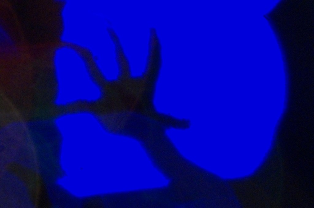 A shadowy hand reaching out against a vibrant blue background, evoking a sense of fear and suspense.